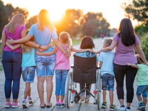 Family and friends hugging each other, including child in wheelchair, showing social support chronic illness in everyday life.