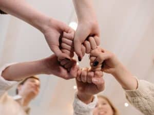 Group of people linking fists together symbolising teamwork and social support chronic illness empowerment in group settings.