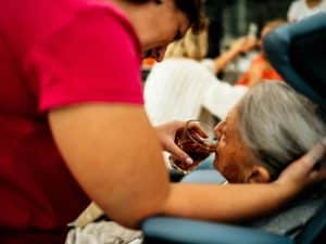 Caregiver helping elderly woman drink water, performing essential personal care tasks for hydration support.