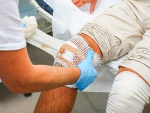 Home wound care nurse applying sterile dressing to an injured knee of a patient in a clinical home setting.