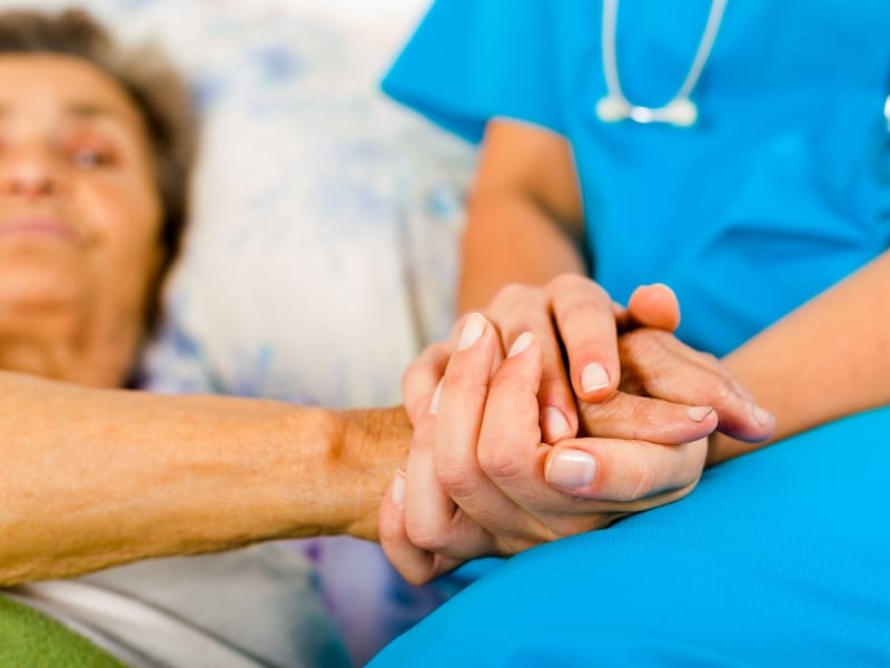 Nurse holding elderly patient's hand while providing emotional support as part of personal care tasks.