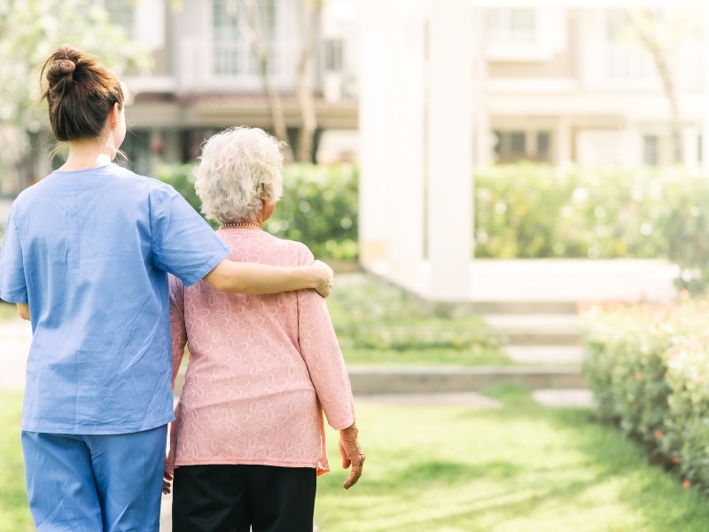 Female caregiver walking with an elderly woman outdoors, symbolising independence and home care comfort through daily companionship