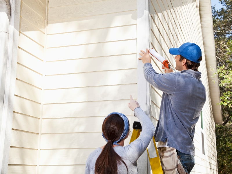 Man sealing exterior wall corner during high quality home maintenance.