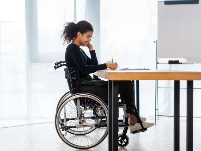 Woman in wheelchair writing confidently with ndis home and living supports.